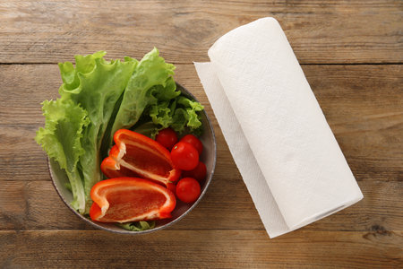 Bowl with fresh vegetables and roll of paper towels on wooden table, flat layの写真素材