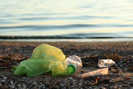 Plastic bag and bottles on sand near water. Environment pollution