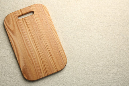 Wooden cutting board on beige table, top view. Space for text