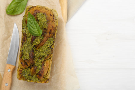Freshly baked pesto bread with basil and knife on white wooden table, flat lay. Space for textの写真素材