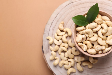 Tasty cashew nuts and green leaves on pale brown background, top view. Space for textの写真素材