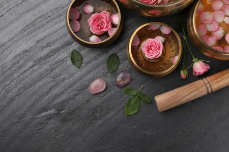 Tibetan singing bowls with water, beautiful rose flowers and mallet on gray table, flat lay. Space for textの写真素材
