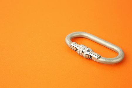 One metal carabiner on orange background, closeup. Space for textの写真素材