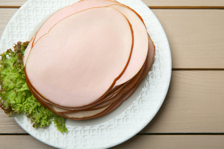 Slices of delicious boiled sausage with lettuce on beige wooden table, top viewの写真素材