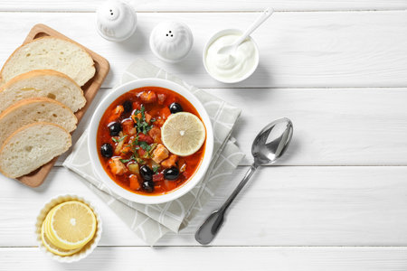 Meat Solyanka soup with sausages, olives and vegetables served on white wooden table, flat lay. Space for textの写真素材