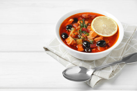 Meat Solyanka soup with sausages, olives, vegetables and spoon on white wooden table, space for textの写真素材