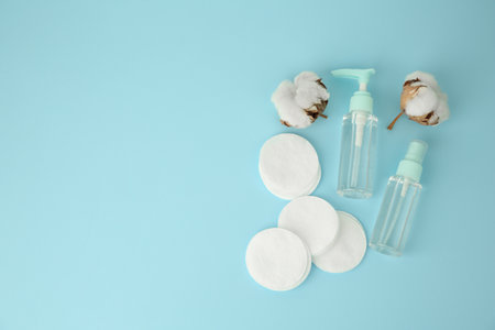 Cosmetic products, cotton pads and flowers on light blue background, flat lay. Space for textの写真素材