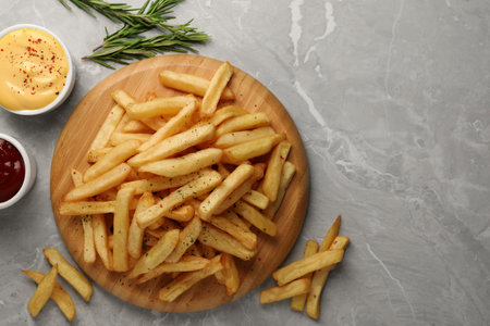 Delicious French fries served with sauces on gray marble table, flat lay. Space for text
