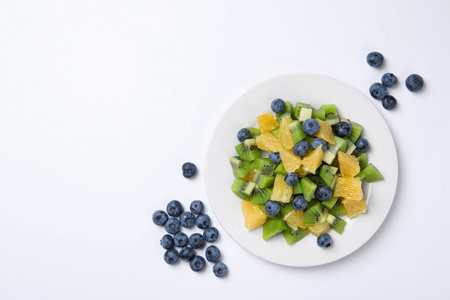 Plate of tasty fruit salad and blueberries on white background, flat lay. Space for textの写真素材