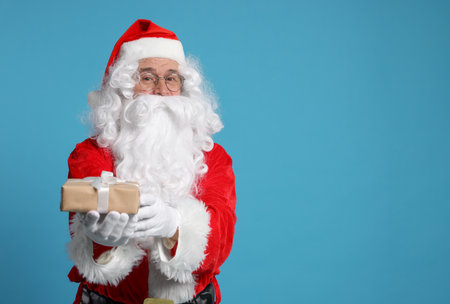 Santa Claus holding Christmas gift on light blue background, space for textの写真素材
