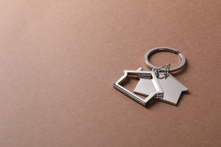 Metallic keychains in shape of houses on light brown background. Space for textの写真素材