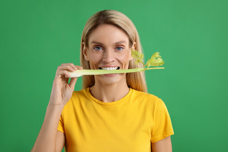Woman eating fresh celery stem on green backgroundの写真素材