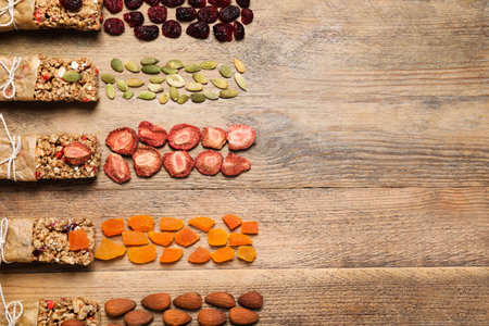 Different tasty granola bars and ingredients on wooden table, flat lay. Space for textの写真素材