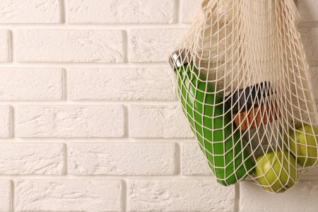 Net bag with different items hanging on brick wall, space for text. Conscious consumptionの写真素材