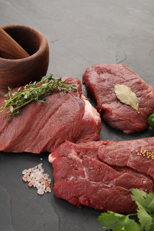Pieces of raw beef meat, mortar with pestle and spices on black tableの写真素材