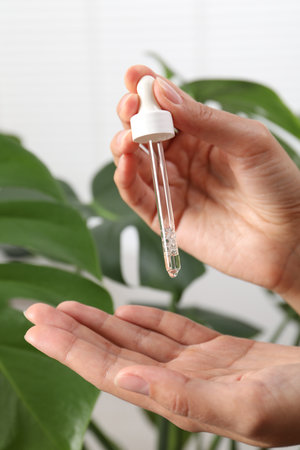 Woman applying cosmetic serum onto her hand near green plant on white background, closeupの写真素材