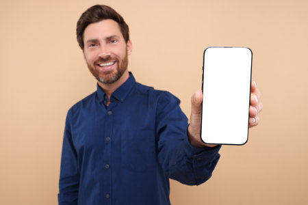 Handsome man showing smartphone in hand on light brown background, selective focus. Mockup for designの写真素材