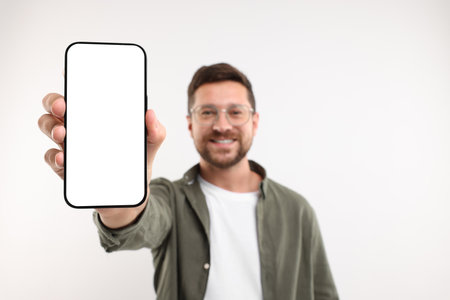 Handsome man showing smartphone in hand on white background, selective focus. Mockup for designの写真素材