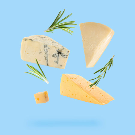 Different kinds of cheese and rosemary falling on light blue backgroundの写真素材