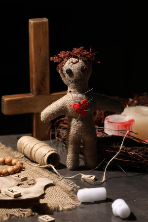 Voodoo doll with pins in heart and ceremonial items on black tableの写真素材