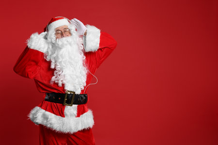 Merry Christmas. Santa Claus in headphones listening to music on red background, space for textの写真素材
