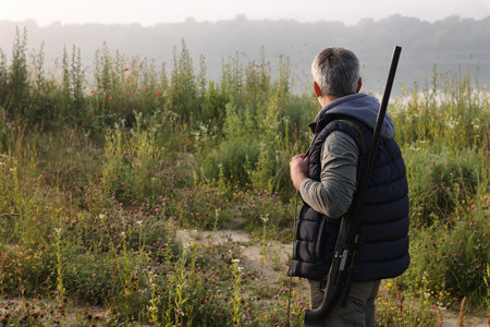 Man with hunting rifle outdoors, back view. Space for text