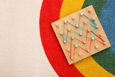 Motor skills development. Wooden geoboard with rubber bands on carpet, top view. Space for textの写真素材