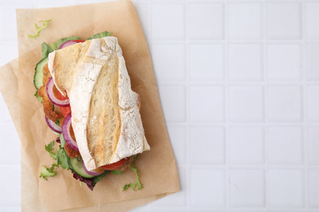 Delicious sandwich with schnitzel on white tiled table, top view. Space for textの写真素材