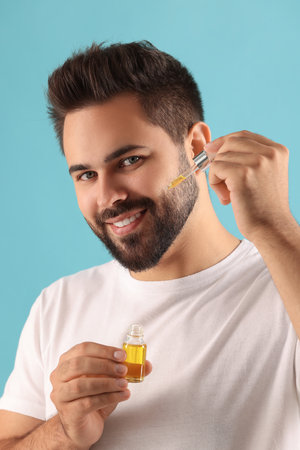Handsome man applying cosmetic serum onto face on light blue backgroundの写真素材