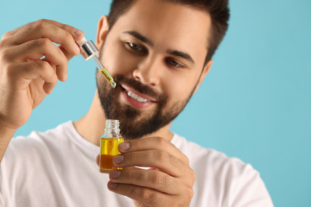 Handsome man with cosmetic serum in hands on light blue background, selective focusの写真素材