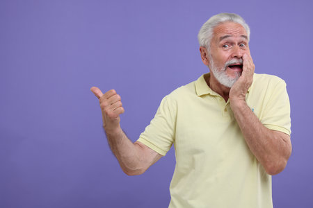 Special promotion. Emotional senior man pointing at something on purple background. Space for textの写真素材