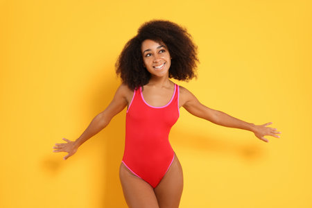 Beautiful woman in bright one-piece summer swimsuit on yellow backgroundの写真素材