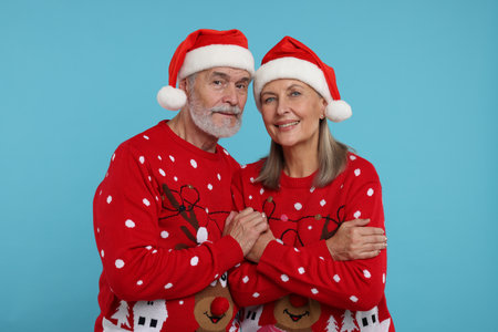 Senior couple in Christmas sweaters and Santa hats on light blue backgroundの写真素材