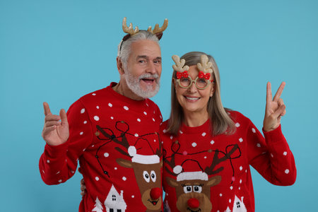Senior couple in Christmas sweaters, reindeer headband and funny glasses on light blue backgroundの写真素材