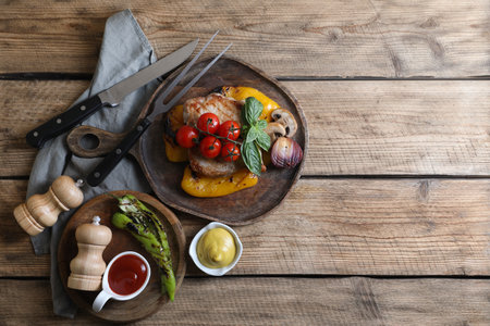 Delicious grilled meat and vegetables served with sauces on wooden table, flat lay. Space for textの写真素材
