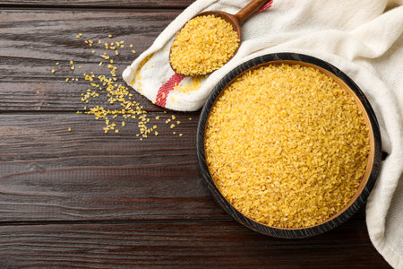 Bowl and spoon with raw bulgur on wooden table, top view. Space for textの写真素材