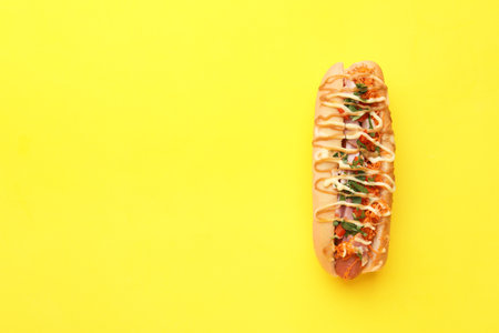 Delicious hot dog with bacon, carrots and parsley on yellow background, top view. Space for textの写真素材