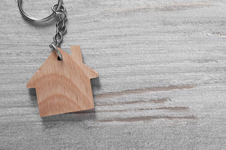 One keychain in shape of house on light wooden table, top view. Space for textの写真素材