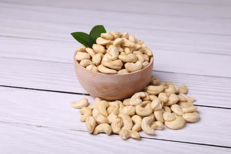 Tasty cashew nuts and green leaves on light wooden tableの写真素材