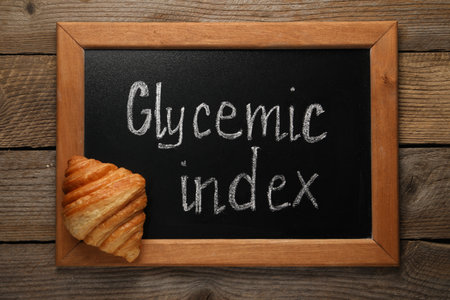 Small chalkboard with words Glycemic Index and croissant on wooden table, top viewの写真素材