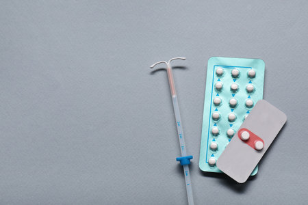 Birth control pills and intrauterine device on light gray background, flat lay and space for text. Choosing method of contraceptionの写真素材