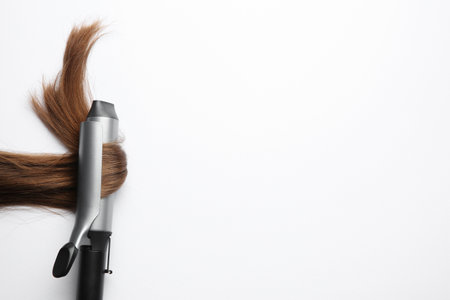Curling iron with brown hair lock on white background, top view. Space for textの写真素材
