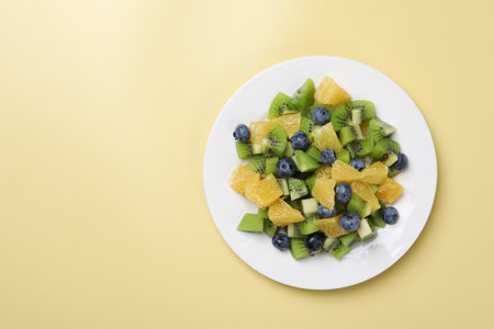 Plate of tasty fruit salad on pale yellow background, top view. Space for textの写真素材