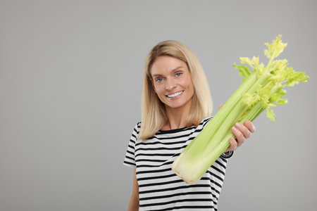 Woman holding fresh green celery bunch on light gray background. Space for textの写真素材