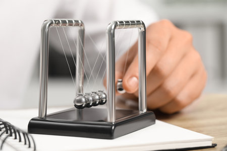 Man playing with Newton's cradle at table, closeup. Physics law of energy conservation