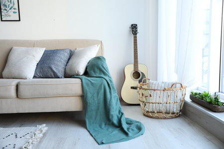 Guitar near comfortable sofa with cushions and plaid in stylish living room interiorの写真素材