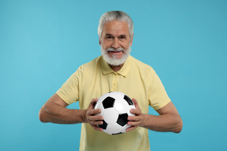 Smiling senior sports fan with soccer ball on light blue backgroundの写真素材