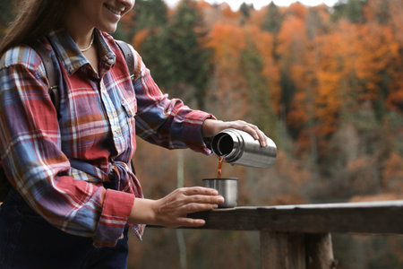 Woman pouring hot drink from metallic thermos into cup lid outdoors, closeup. Space for textの写真素材