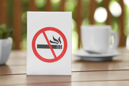 No Smoking sign and cup of drink on wooden table against blurred background, closeupの写真素材