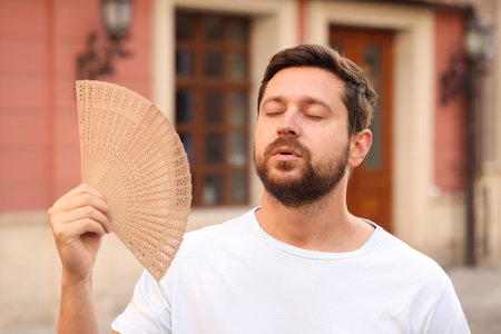 Man with hand fan suffering from heat outdoorsの写真素材